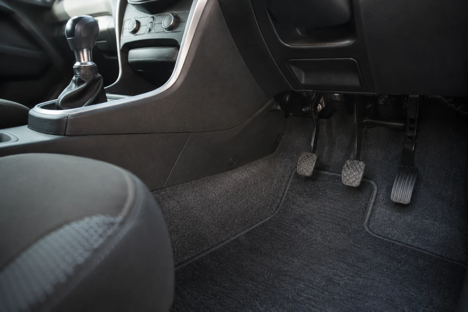 The footwell and gear lever of a manual car, showing the clutch, brake and accelerator pedals