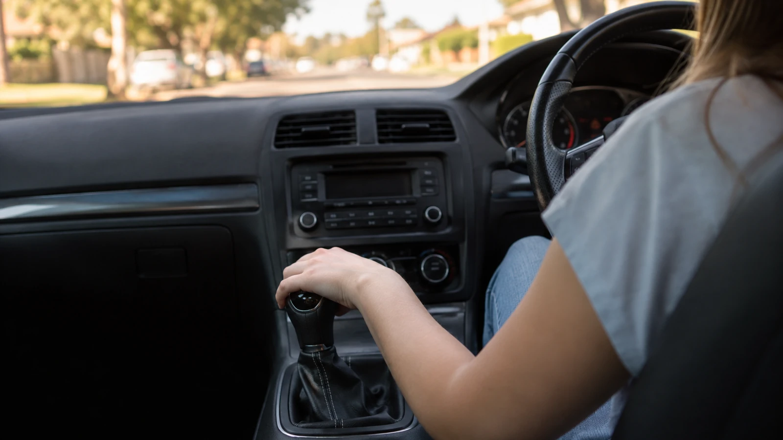 A learner driver's left hand on the gear lever of a manual car during a driving lesson