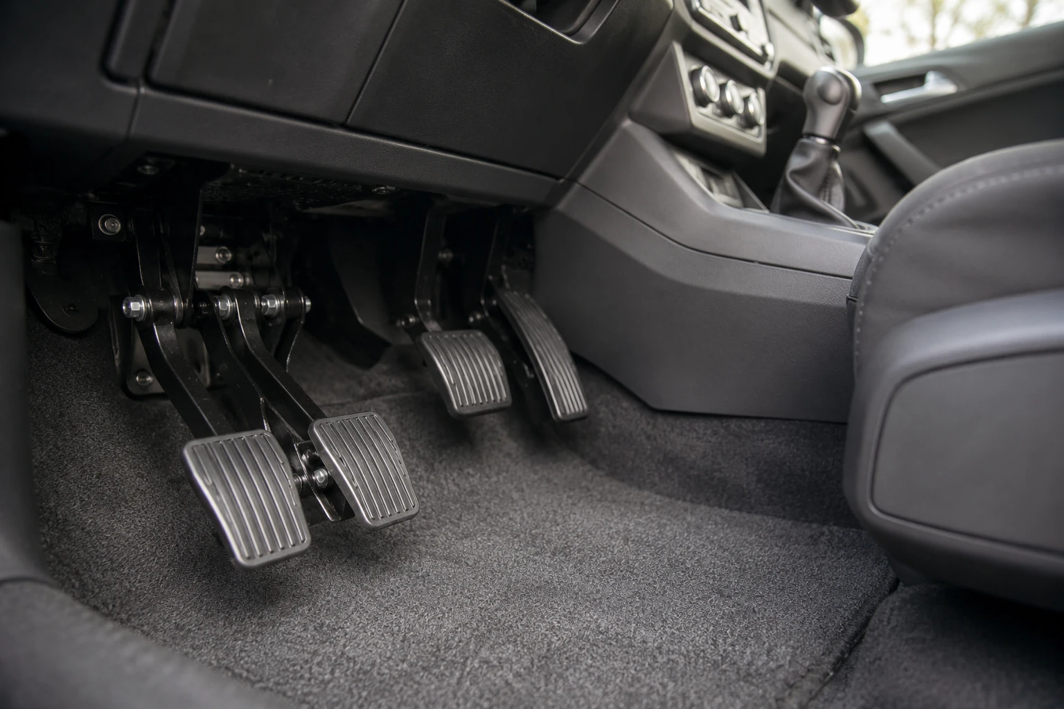 Interior view of a dual-control driving school car showing the instructor's second set of pedals
